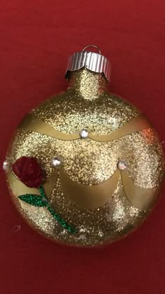 a gold ornament with a red rose on it sitting on a red surface