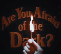 a hand holding a lit matchstick with the words are you afraid of the dark?