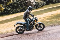 a man riding on the back of a motorcycle down a dirt road next to trees