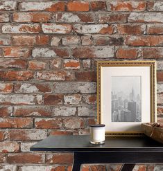 an old brick wall with a picture frame and coffee cup on the table next to it