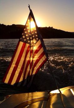 an american flag is on the back of a boat in the water at sunset or dawn