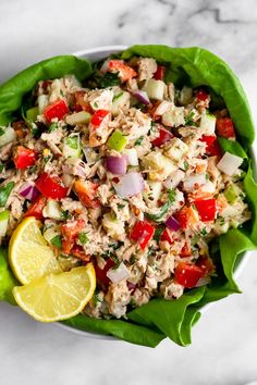 a salad in a bowl with lettuce, tomatoes, onion and lemon wedges