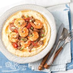 a white bowl filled with shrimp and grita on top of a blue napkin next to silverware