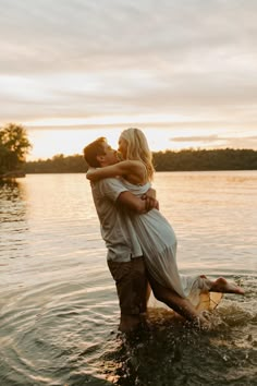 a man and woman are hugging in the water at sunset on a lake with their arms around each other