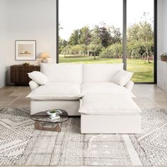 a living room with a white sectional couch and coffee table in front of large windows