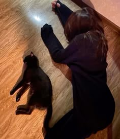 a woman laying on the floor next to a black cat with it's head under her leg