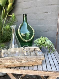 a wooden table topped with green vases and glasses next to succulents