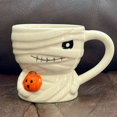 a white coffee cup with an orange pumpkin in it's mouth on a couch