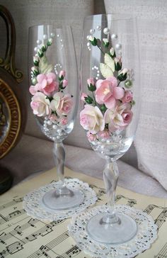 two wine glasses with flowers on them sitting next to each other in front of sheet music