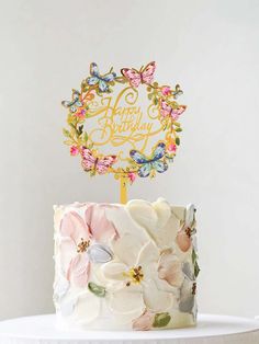 a birthday cake decorated with flowers and butterflies on a white table next to a candle