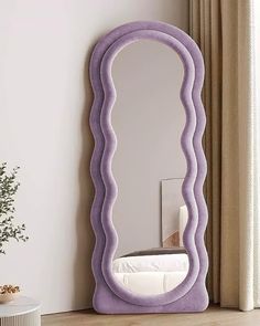 a large purple mirror sitting on top of a wooden floor next to a white table