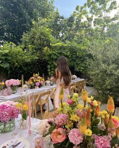 a woman sitting at a table with flowers in vases and plates on the table