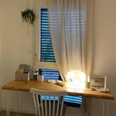 a desk with a lamp on it in front of a window and a chair next to it