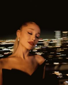 a woman with her eyes closed standing in front of a cityscape at night