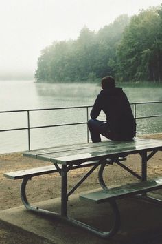 a person sitting at a picnic table looking out over the water on a foggy day