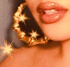 a close up of a woman's face wearing large gold hoop earrings with stars on them