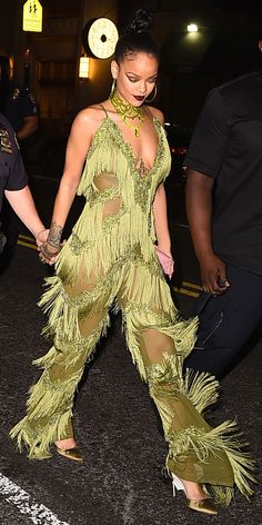 a woman in a green outfit walking down the street with her hand on her hip