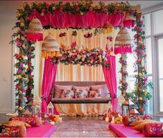 a decorated stage with pink and yellow draping, flowers on the ceiling, and lots of pillows