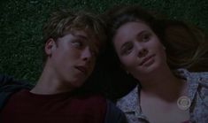 a young man and woman laying next to each other on the grass with their eyes closed