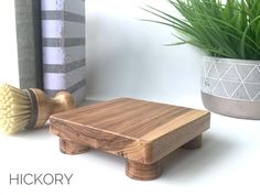 a wooden stool next to a potted plant on a white table with the words hickory written below it