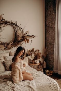 a woman sitting on top of a bed next to a wall with dried plants in it