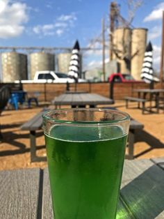 a green drink sitting on top of a wooden table next to picnic tables in the background