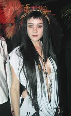 a woman with long black hair wearing a white shirt and a crown on her head