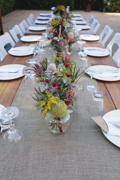 a long table with white plates and flowers in vases