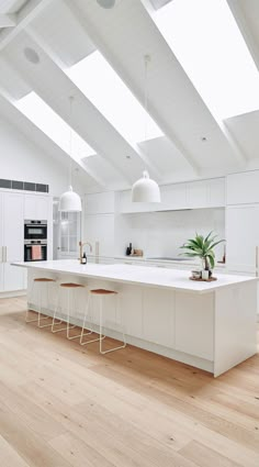 an open kitchen with white cabinets and counter tops, along with bar stools that match the hardwood flooring