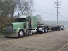 a green semi truck is parked on the side of the road with power lines in the background