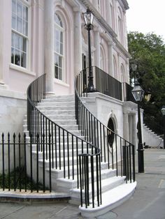 a black wrought iron staircase next to a pink building with white columns and windows on both sides