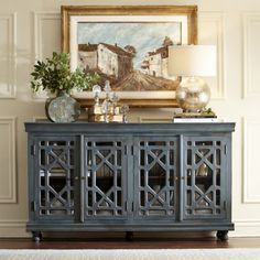 an ornately decorated sideboard stands in front of a painting and lamp on the wall