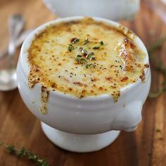 two white bowls filled with food sitting on top of a wooden table next to spoons