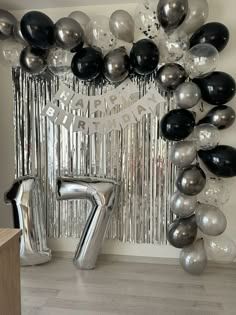 the number seven balloon arch is decorated with black and silver balloons, streamers and confetti