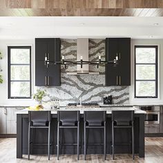 a kitchen with black cabinets and white marble counter tops, along with bar stools