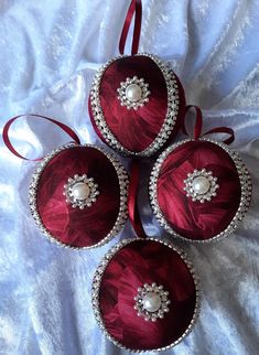 four red ornaments with pearls on them sitting on a white sheet