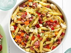 a bowl filled with pasta and vegetables on top of a table next to a plate of salad