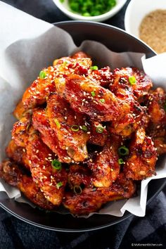 a bowl filled with chicken wings covered in sauce and green onions