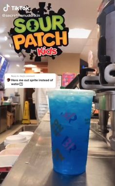 a blue drink sitting on top of a counter in front of a coffee machine with the words sour patch kids written on it