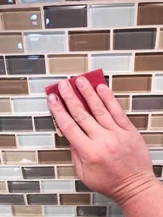 a woman's hand holding a sponge on top of a tile backsplash