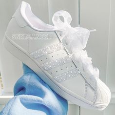 a white adidas sneaker with pearls on the side and a blue sock next to it