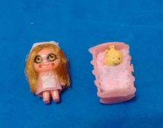 a doll with glasses is next to a small plastic toothbrush holder on a blue surface