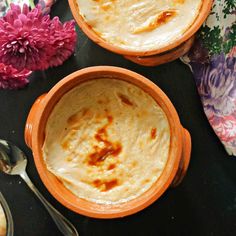 two orange bowls filled with food on top of a black table next to pink flowers