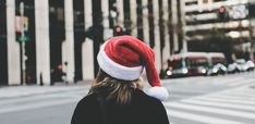 a woman wearing a santa hat while standing on the side of a road in front of tall buildings