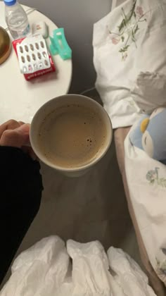 a person is holding a cup of coffee in their hand while sitting on a bed