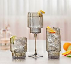 three glasses on a table with oranges, cucumbers and lemon wedges