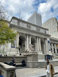 people are walking around in front of an old building with columns and lions on it