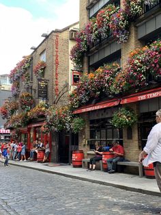 people are walking down the street in front of buildings with flowers growing on it's windows