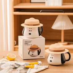 two ceramic mugs sitting on top of a table next to a box with an image of a penguin