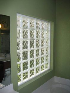 a bathroom with green walls and a white tub in front of a window that has glass blocks on it